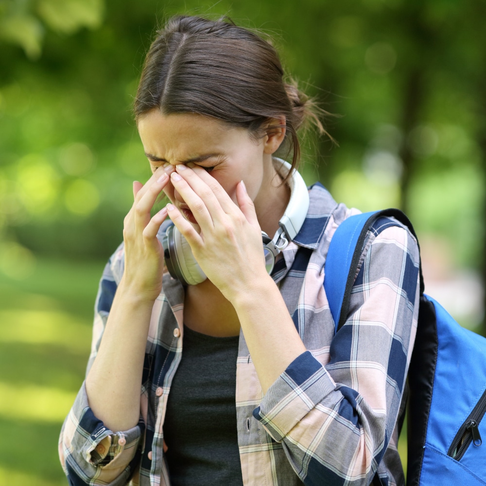 a student walking outdoors pushes on the bridge of her nose