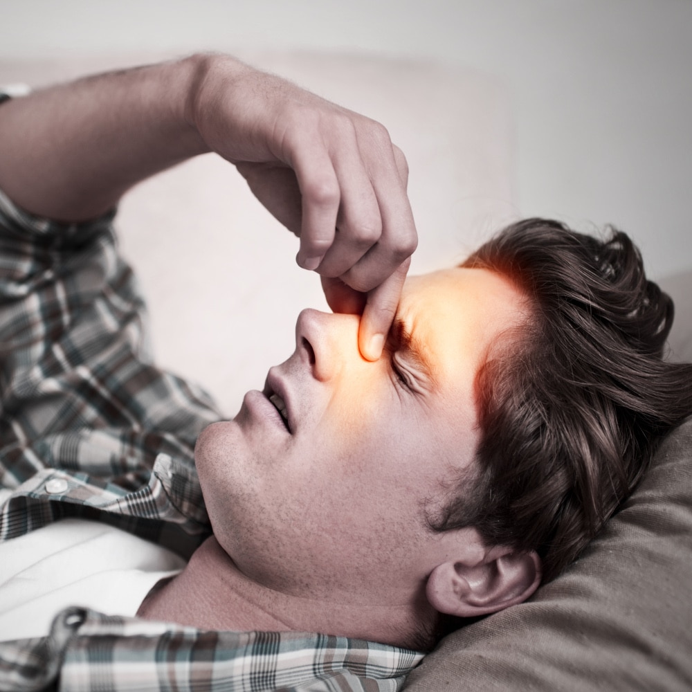 A young man holds his head as he lays on a couch